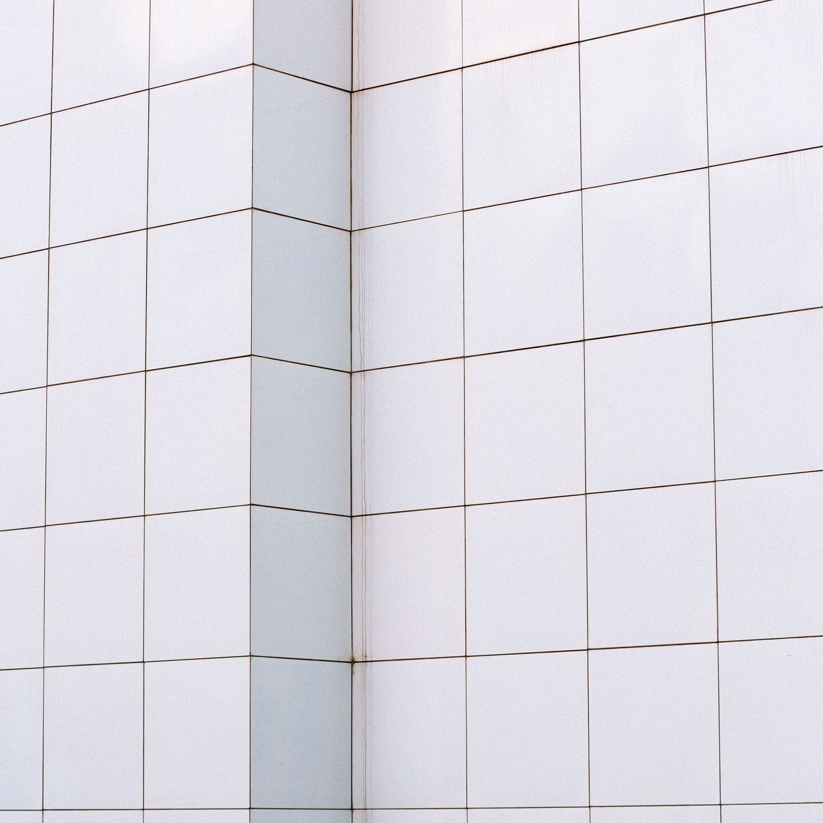 Angle de mur en faïence blanche où les joints continuent d’une face à l’autre sans décalage