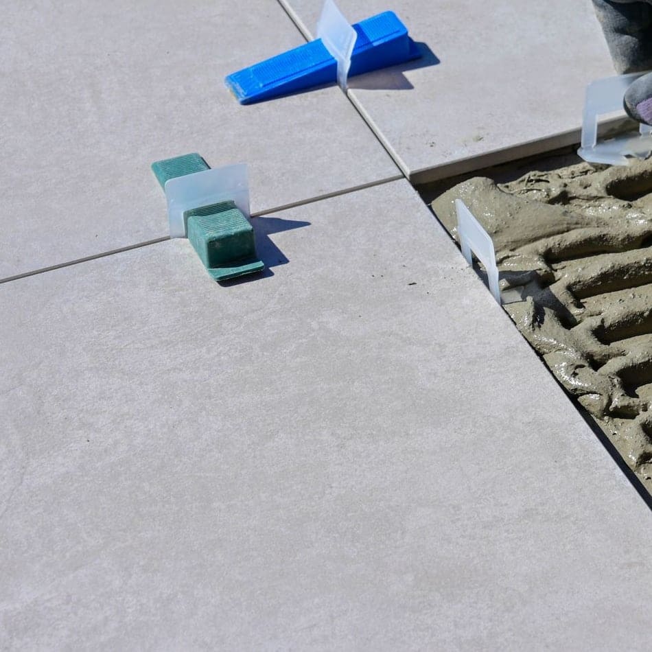 Colle étalée au peigne à côté d’un carreau posé, avec croisillons et cales de nivellement